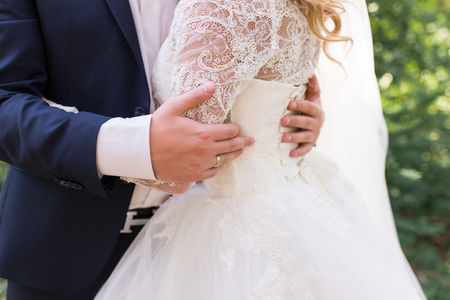 Happy bride and groom holding each other and walking in nature on wedding day. Wedding couple in love, newlyweds, free space. Bride in white dress and groom in blue suit outdoorsの写真素材