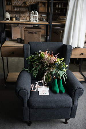 Rich green wedding bouquet with pink ribbons on the gray armchair. Green bridal shoes, and a wedding complimentary lacing near the bridal lush bouquet. Detailsの写真素材