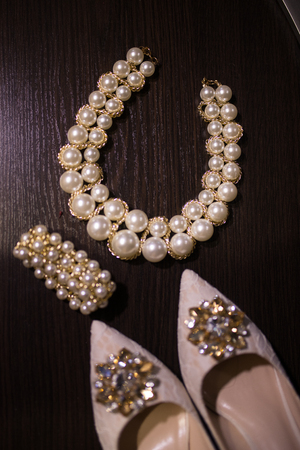 Beautiful set of women's wedding accessories. Pearl necklace in focus, beige shoes with shiny stones on them, and a bracelet on the wooden background.の写真素材