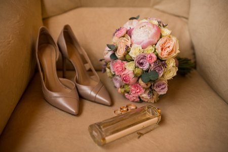 Wedding bouquet with pink peony, yellow roses and greenery with elegant bridal shoes, wedding rings and perfume. Wedding detailsの写真素材