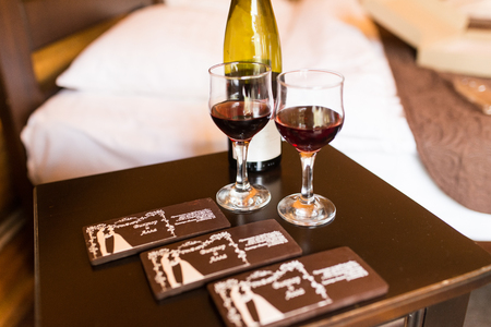 Two glasses are filled with red wine. Near the wineglasses stand a bottle of wine and a few chocolates lying.の写真素材