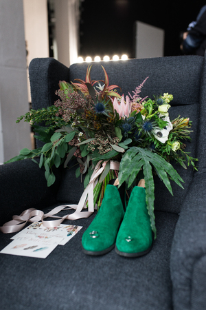 Rich green wedding bouquet with pink ribbons on the gray armchair. Green bridal shoes, and a wedding complimentary lacing near the bridal lush bouquet. Detailsの写真素材