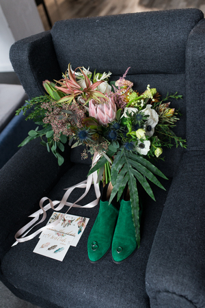 Rich green wedding bouquet with pink ribbons on the gray armchair. Green bridal shoes, and a wedding complimentary lacing near the bridal lush bouquet. Detailsの写真素材