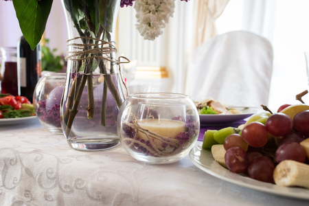 Beige candle in a glass vase with lilac petals. Wedding decor on the table at the newlywedsの写真素材