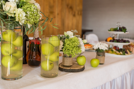 Rustic flower arrangement with white flowers and greenery in a glass vase with water and apples at a wedding banquet. Table set for an event party or wedding reception.の写真素材