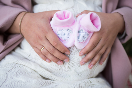Pregnant woman holding a small pink pair of booties over her bare belly. Future mother knows a sex of her baby. Pregnancy concept.の写真素材