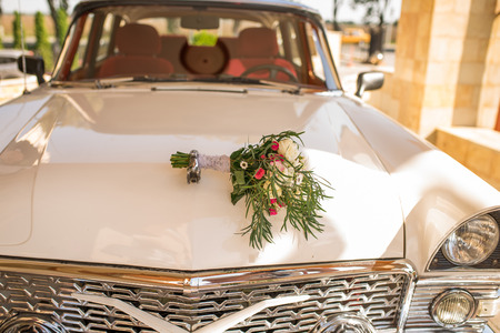 Lush bridal bouquet with white and pink flowers with a lot of greenery lying on the hood of white car of bride and groom.の写真素材