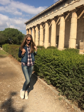 Smiling Caucasian girl in sunglasses. A girl with long hair in a denim suit and white sneakers the girl walking along the ancient temple with columns. Summertimeの写真素材