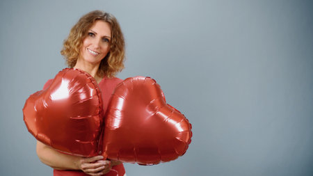 A woman with a red heart in the shape of a balloon smiles on a gray background.の写真素材