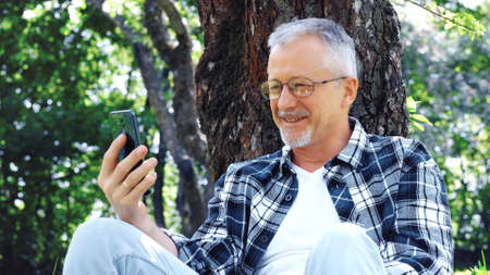 An elderly gray-haired slender man with glasses talks on the phone and enjoys the fresh air and...