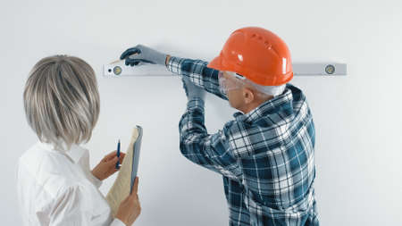 An elderly worker in a hard hat and a gray-haired female engineer with a tablet in their hands are discussing plans for the reconstruction of the facility. Making decisions on repairs.の写真素材