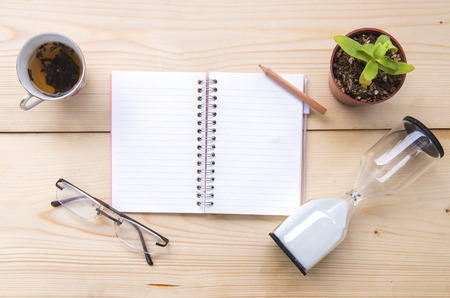 A notebook placed on a wooden table with glasses, hourglasses, tea cups and small trees in a potの写真素材