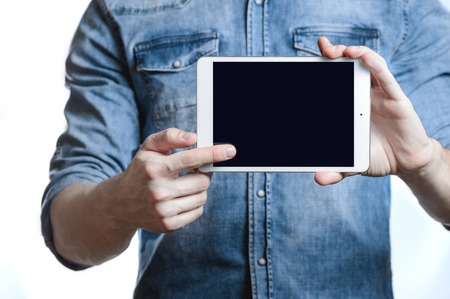 Casual man in denim shirt showing digital tablet computer screen in hands. Isolated on white....