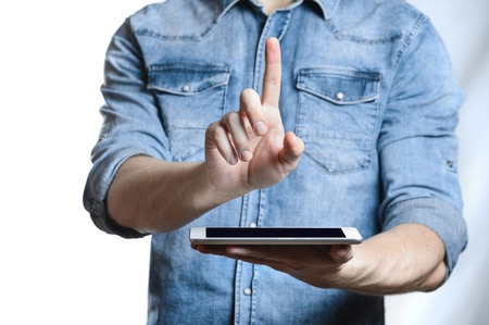 Casual man in denim shirt showing digital tablet computer screen in hands. Isolated on white. Clipping path for display included. He points a finger at the display.の写真素材