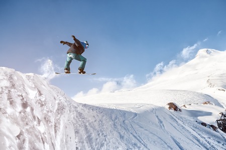 Stylish snowboarder with helmet and mask jumps from high snow slopeの写真素材