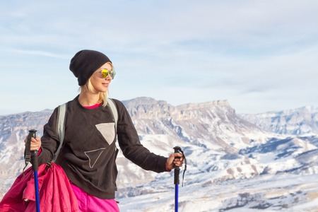 Young beautiful girl in sunglasses with Nordic poles in the sunset light on the background of the Caucasian ridgeの写真素材