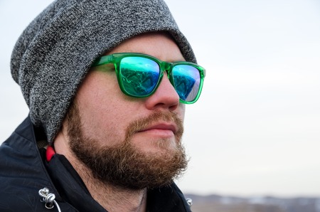 Young bearded hipster wearing a hat and sunglasses with Nordic walking sticks and a backpack moves in the mountains at sunset, against a background of sunset sky and volcano Elbrusの写真素材
