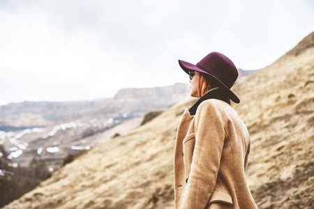 A girl in a classic style, a hat and coat in the mountains in a foggy evening