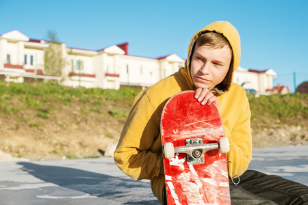Close-up of a teenager dressed in a jeans hoodie sitting in a skate park and holding a skateboardの写真素材