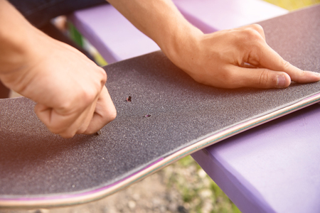 Boy makes bolt holes on the griptape on a skateboardの写真素材
