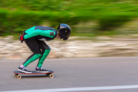 A young man in helmet and a leather suit in a special rack rides a longboard on afsaltu on background mountains and beautiful skyの写真素材