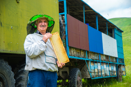 A beekeeper man holds a frame with honeycomb-filled honeycombsの写真素材