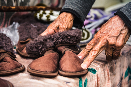 Old wrinkled female hands hold childrens shoesの写真素材