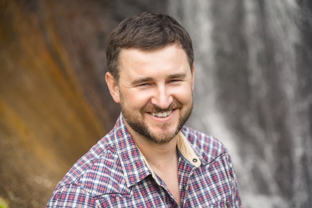 Close-up portrait of a bearded smiling hipster against a waterfall backgroundの写真素材