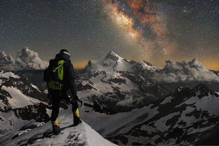 Night photo climber stands on top of a mountain in the snow and looks at the surrounding mountains...