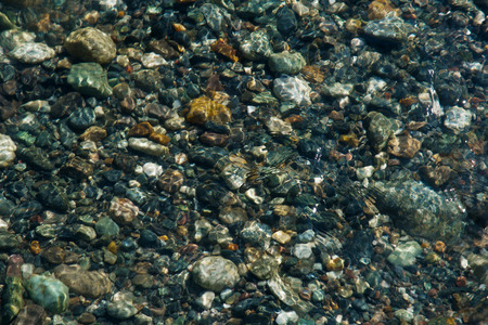 small multicolored stones on the bank of a mountain stream with crystal clear glacial water. Top...