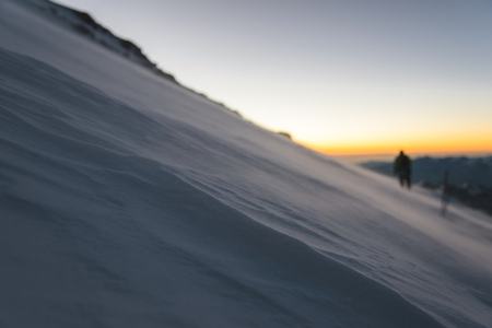 blurred climber at sunrise early morning walks on the slope and on the ground above the snow sweeps drifting snowの写真素材