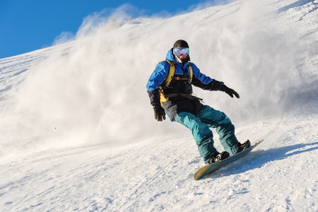 Freeride snowboarder rolls on a snow-covered slope leaving behind a snow powder against the blue skyの写真素材