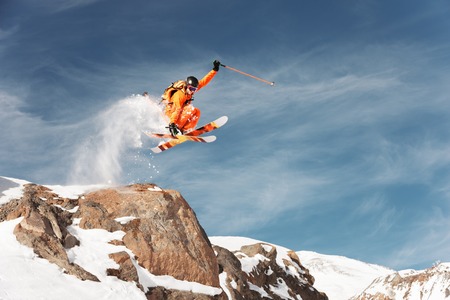 An athlete skier is jumping from high rock high in the mountains.の写真素材
