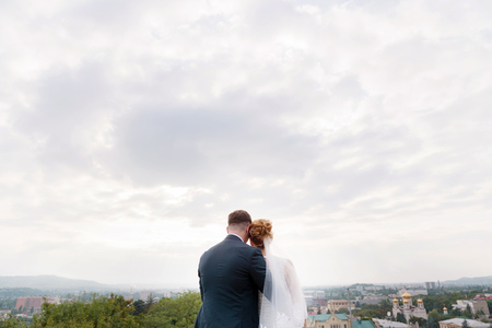 A loving couple of newlyweds stand holding hands and embracing against the background of the city landscape of the resort city in the northern Caucasus.の写真素材