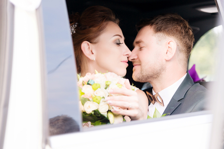 Portrait of a young kissing couple in love with a newlywed couple next to a bouquet in the window of a wedding car.の写真素材