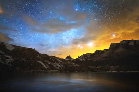 High mountain lake in the northern Caucasus, surrounded by epic rocks and a bright winter starry sky at sunset. Night scenery on long exposure. Magic pictureの写真素材