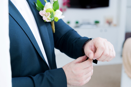 A stout bridegroom with a beard in a suit adjusts the sleeve of his jacket. Super close-up.の写真素材