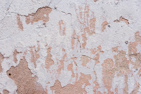 Textured background white cracked plaster partially sprinkled with a pink shaded cracked wall....