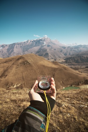 Viewpoint shot. A first-person view of a mans hand holds a compass against the background of an epic landscape with cliffs hills and a blue sky with cloudsの写真素材