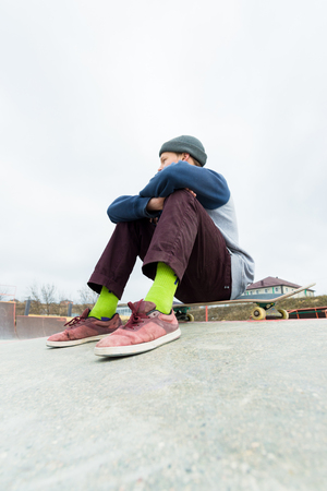 A teenage boy is sitting on a skateboard in the park. The concept of free time pastime for teenagers in the cityの写真素材