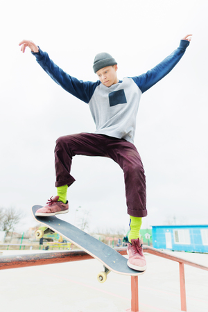 A young teenager, a skateboarder, does a trick on the railing in a skatepark. The concept of youth sports in urban cultureの写真素材