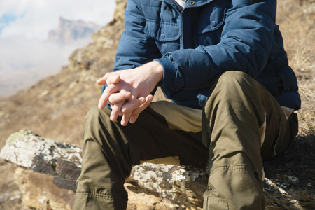 Close-up without a face sitting hipster on a stone high in the mountains against the background of epic rocks. The concept of relaxation in the mountainsの写真素材