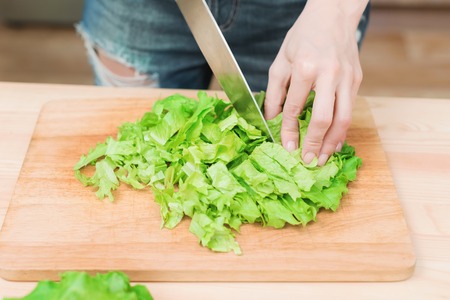 Close-up Female hands chopping a green plant salad cooking salad from vegetables on a wooden cutting board at home. The concept of vegetarianism and healthy lifestylesの写真素材