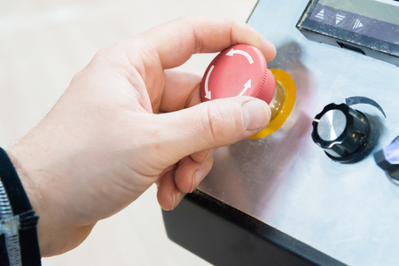 Close-up of a mans hand on a red button on the control panel. Emergency stop or start of equipment...