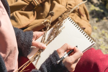 Close-up on the hands of a girl holding a blank notebook. A dry bouquet of herbs in her hand and a pencil. Travel designer artistの写真素材