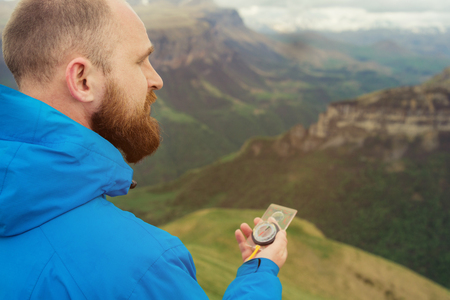 Hipster man in a blue jacket using a compass on the background in the background of the Caucasian landscape with a plateauの写真素材