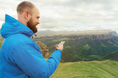 Hipster man in a blue jacket using a compass on the background in the background of the Caucasian landscape with a plateauの写真素材