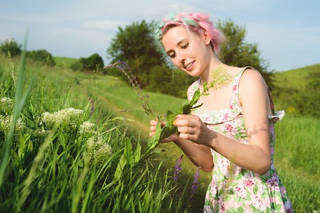 Portrait of a happy young cute girl with multi-colored hair collects flowers next to a country road at sunset. The concept of human harmony with the nature of spring and happinessの写真素材