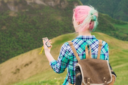 A hipster girl traveled with a blogger in a plaid shirt and with multi-colored hair using a compass in the background in the background of the Caucasian landscape with a plateauの写真素材