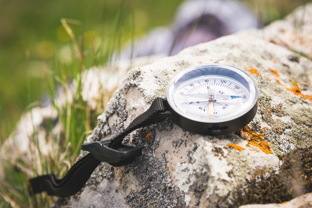 A magnetic compass lies on a stone next to the grassの写真素材